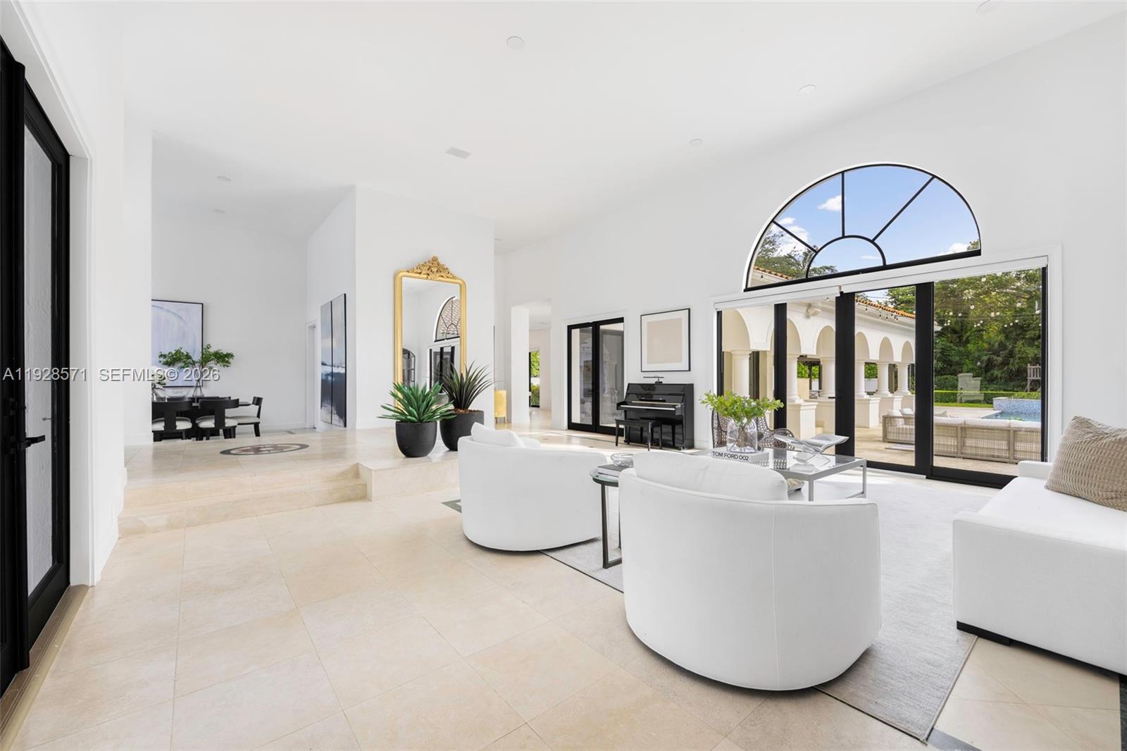 A bright, open-concept living room features white furniture, a grand piano, and large arched windows — 7430 SW 66th St, Miami FL 33143, MIAMI, FL