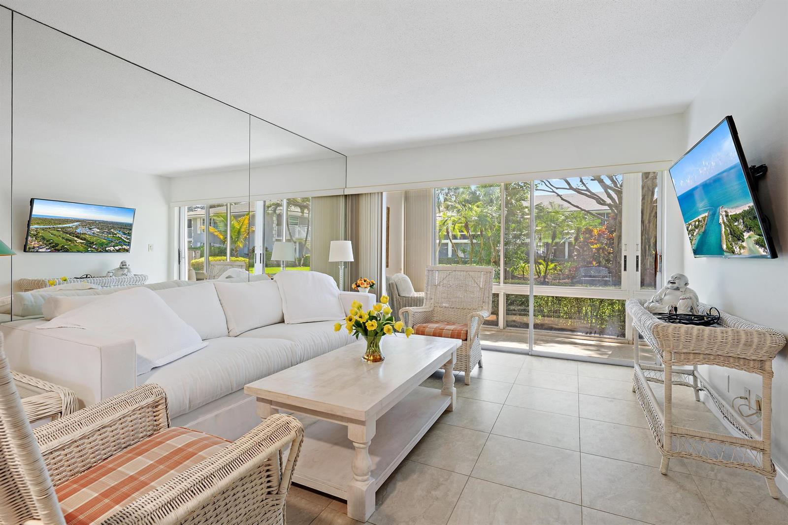 A bright living room features a white sofa, wicker chairs, a coffee table, and mirrored walls — 50 Celestial Way # 105, Juno Beach FL 33408, JUNO BEACH, FL