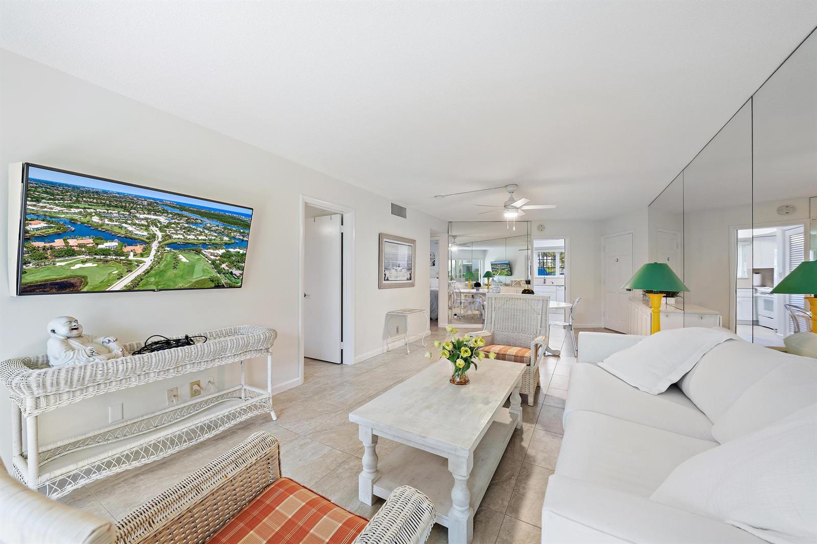 A living room features white wicker furniture, a coffee table, and a wall-mounted television — 50 Celestial Way # 105, Juno Beach FL 33408, JUNO BEACH, FL