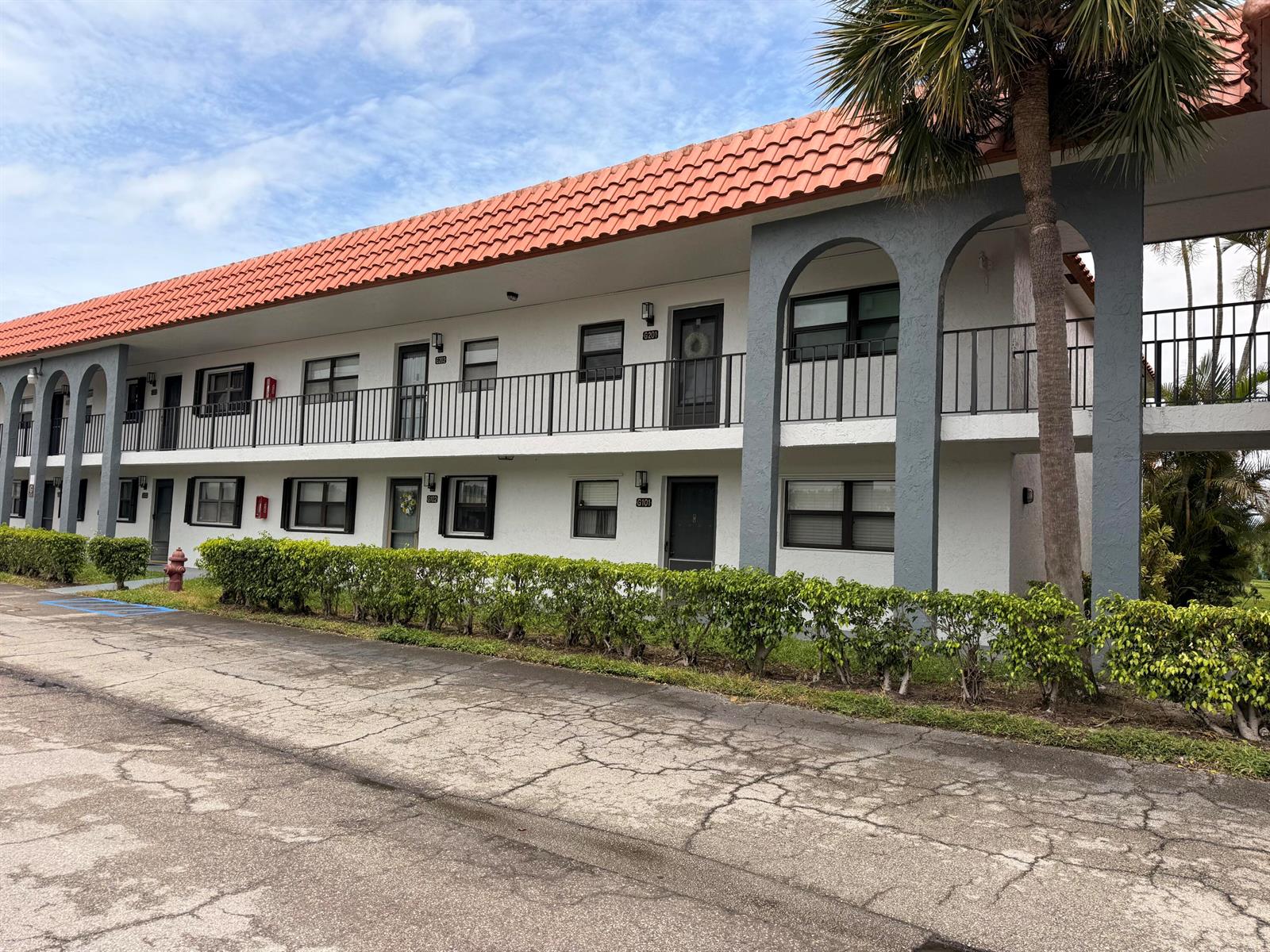 A two-story apartment building features a red tile roof, white stucco walls, and arched columns — 2021 W Woolbright Road # G205, Boynton Beach FL 33426, BOYNTON BEACH, FL