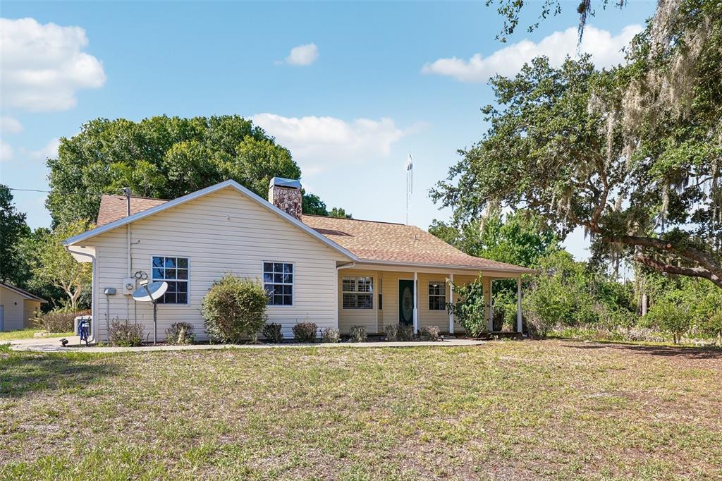 A single-story house with light-colored siding, a stone chimney, and a covered front porch — 204 JEFFERSON DRIVE, LAKE PLACID, FL