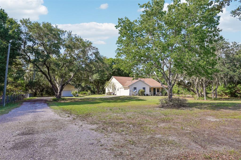 A single-story house with a gravel driveway and a detached garage surrounded by large trees — 204 JEFFERSON DRIVE, LAKE PLACID, FL