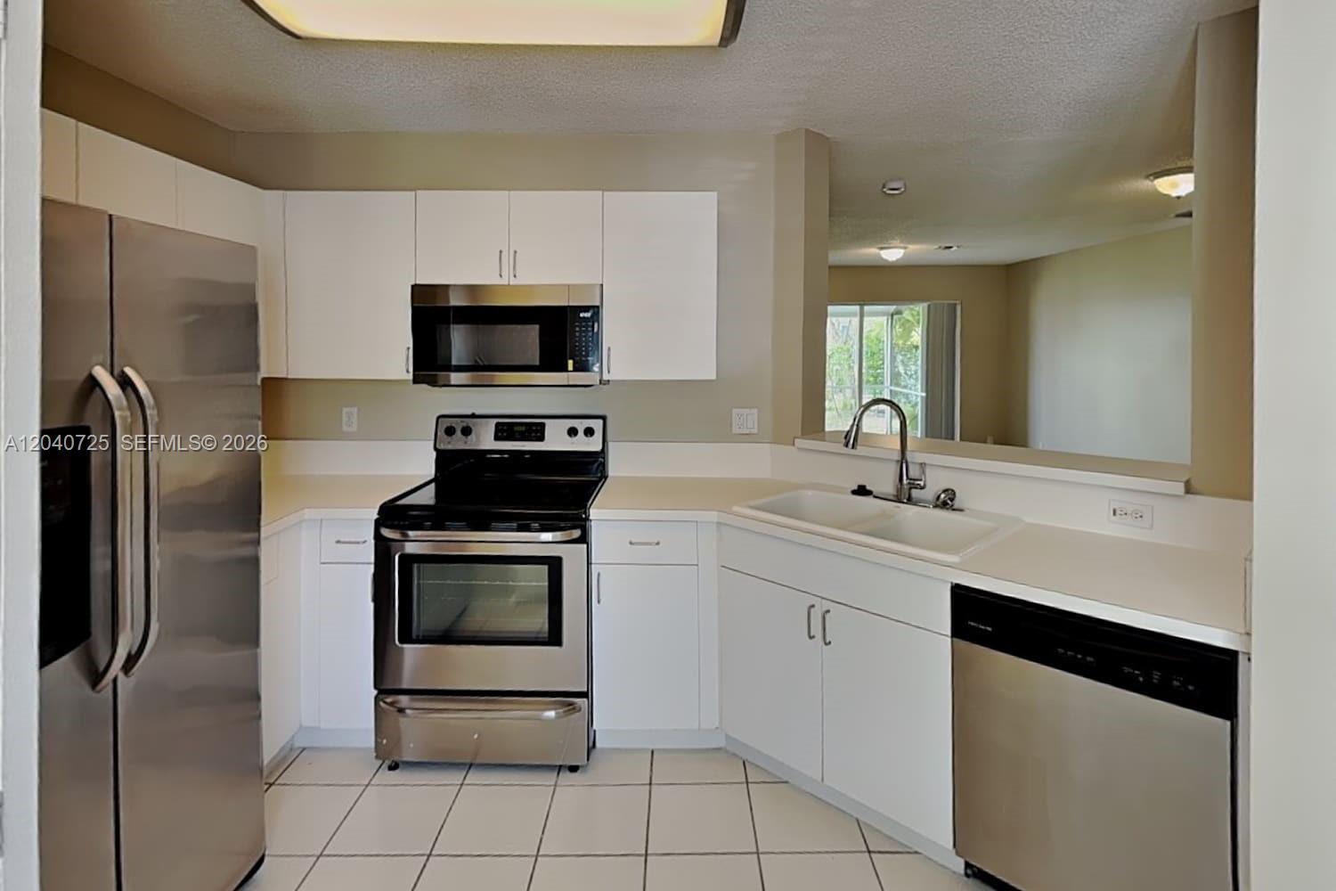 A kitchen features white cabinets, stainless steel appliances, white countertops, and white tile flooring — DEERFIELD BEACH, FL