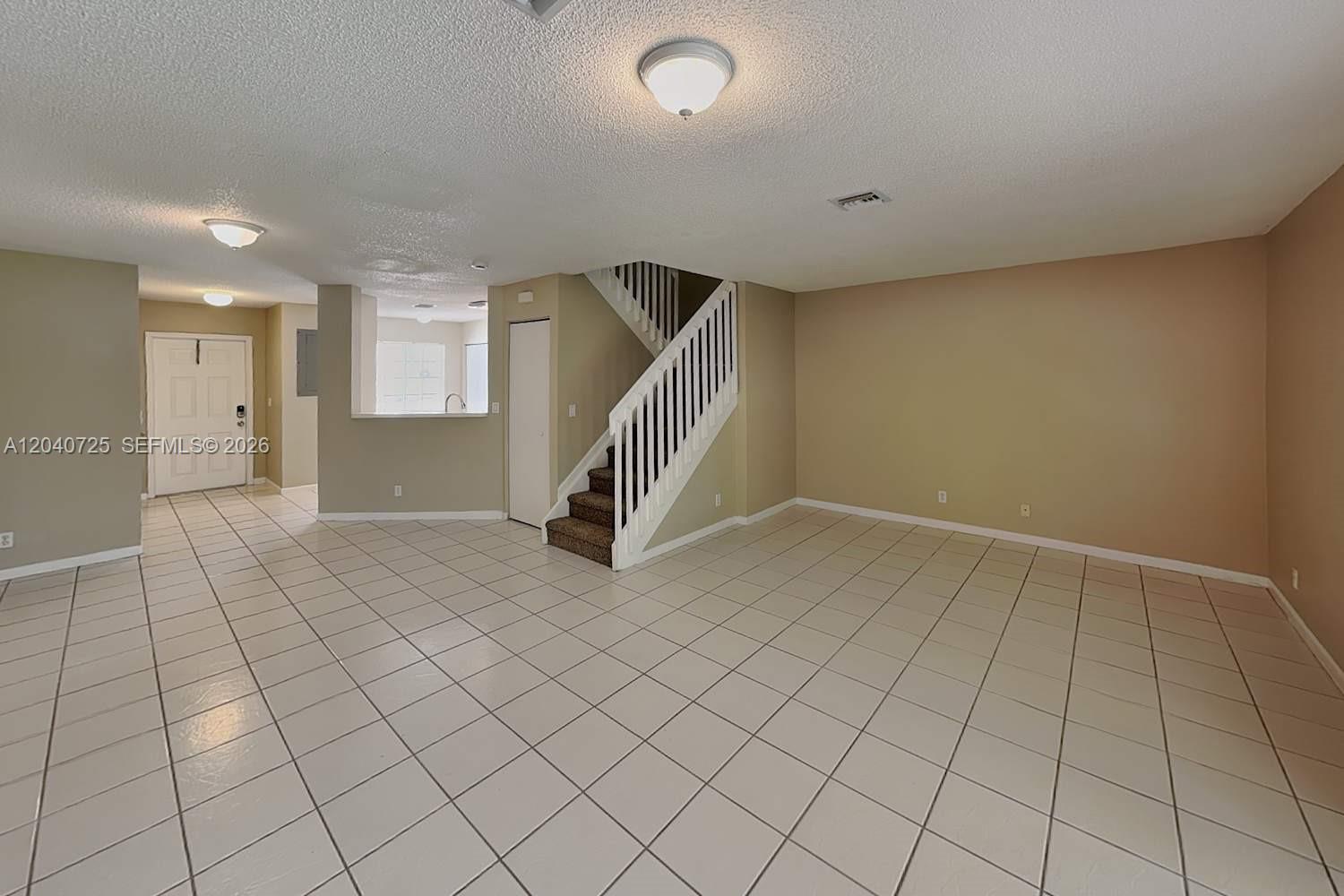 An empty room features beige walls, white tile flooring, and a staircase with white railings — DEERFIELD BEACH, FL