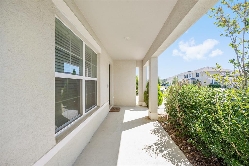 A covered concrete porch features a large window, white stucco walls, and a small doormat — 5394 SW 40TH CIRCLE, OCALA, FL