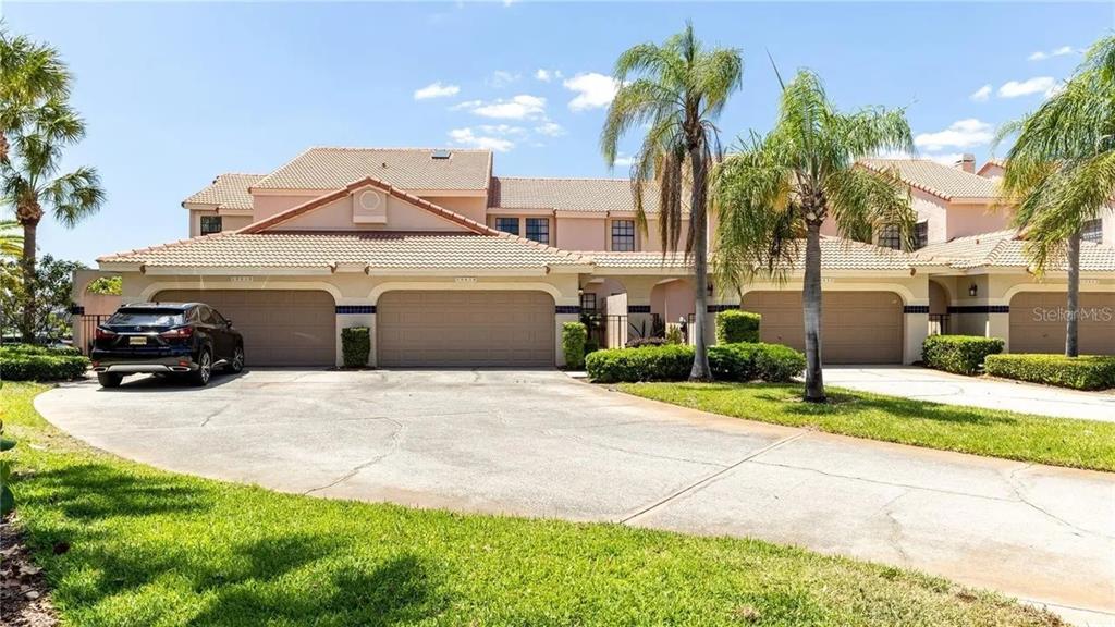 A beige multi-unit residential building features multiple garage doors and a shared concrete driveway — 10438 SAINT TROPEZ PLACE, TAMPA, FL