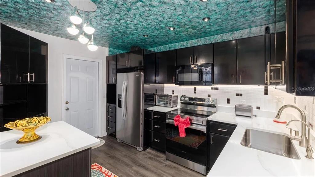 A kitchen features black cabinets, white countertops, stainless steel appliances, and a textured teal ceiling — 10438 SAINT TROPEZ PLACE, TAMPA, FL