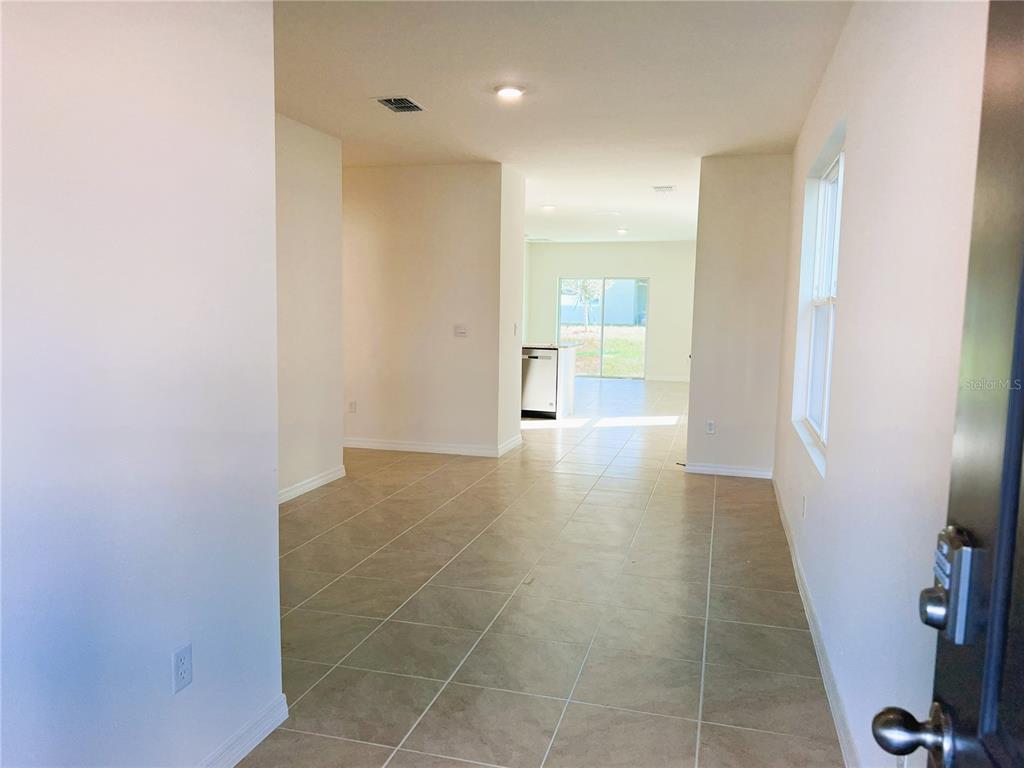 An interior view shows a tiled entryway leading toward an open kitchen and sliding glass doors — 2127 DESERT ROSE DRIVE, DAVENPORT, FL