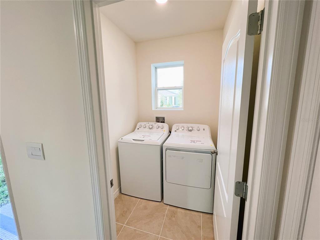 A laundry room features a white washer and dryer, a window, and tiled flooring — 2127 DESERT ROSE DRIVE, DAVENPORT, FL