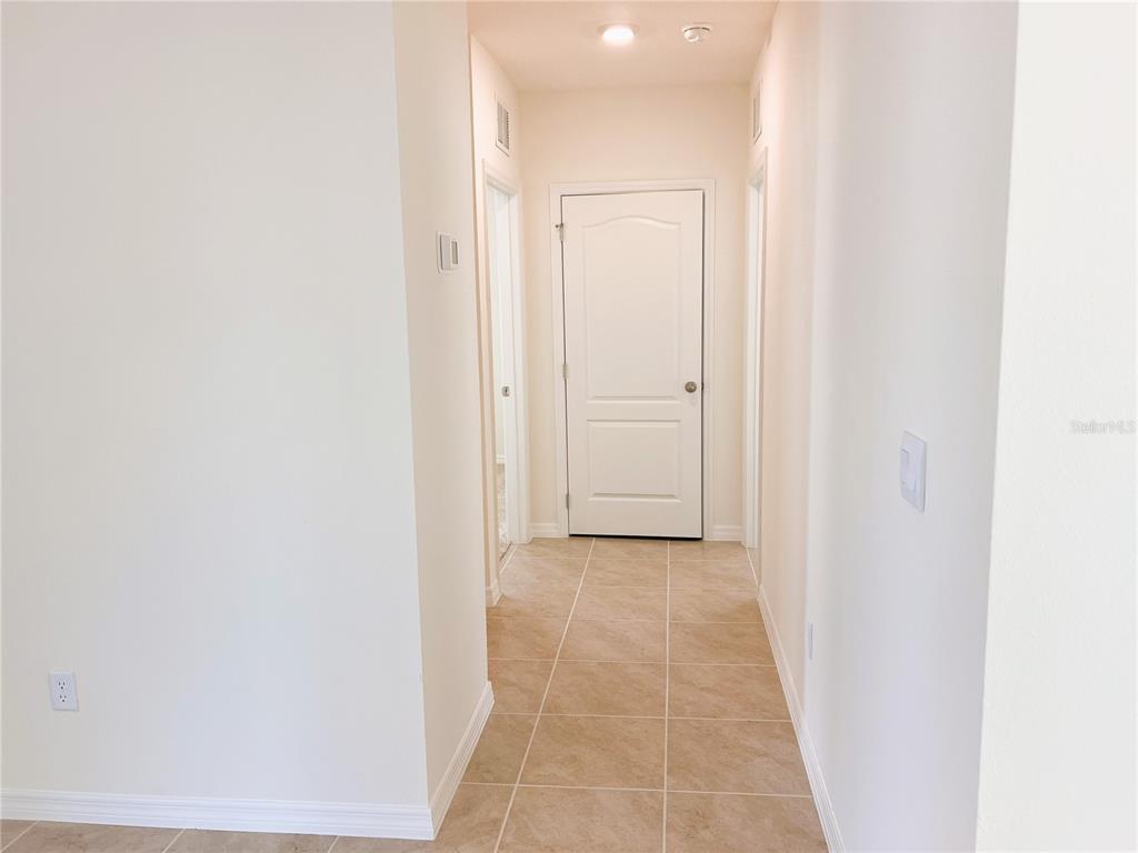 A hallway with beige tile flooring leads to a closed white door — 2127 DESERT ROSE DRIVE, DAVENPORT, FL