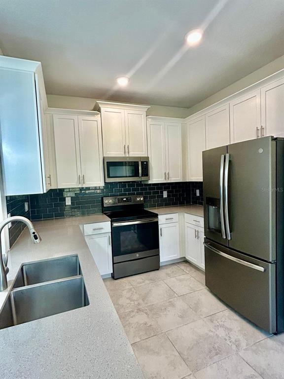 A kitchen features white cabinets, dark subway tile backsplash, stainless steel appliances, and tile flooring — 11576 WHISTLING PINE WAY, ORLANDO, FL