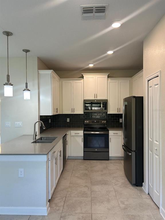A kitchen features white cabinets, dark tile backsplash, stainless steel appliances, and a gray countertop — 11576 WHISTLING PINE WAY, ORLANDO, FL
