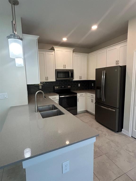 A kitchen features white cabinets, gray countertops, a dark tile backsplash, and stainless steel appliances — 11576 WHISTLING PINE WAY, ORLANDO, FL