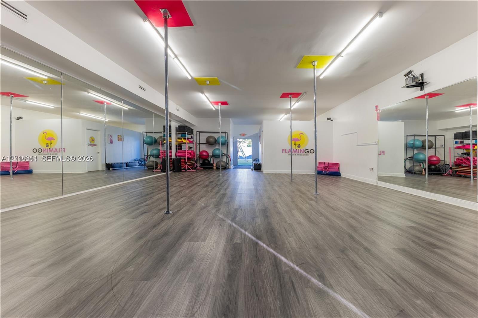 A dance studio features mirrored walls, multiple vertical poles, and gray wood-look flooring — 727 S 21st Ave, Hollywood FL 33020, HOLLYWOOD, FL