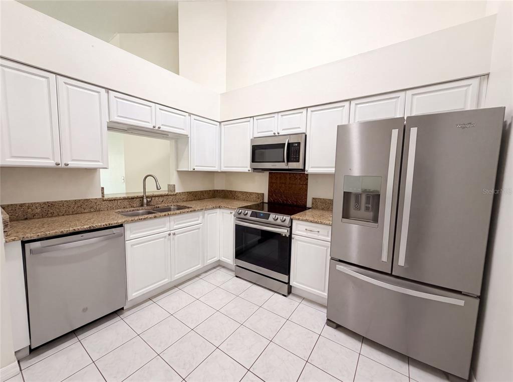 A kitchen features white cabinets, granite countertops, stainless steel appliances, and white tile flooring — 11648 HIDDEN HOLLOW CIRCLE, TAMPA, FL