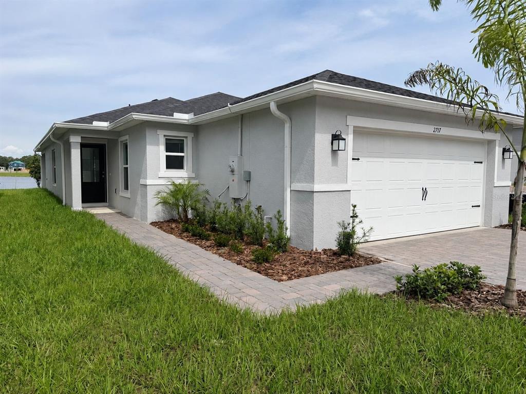 A single-story gray stucco house with a white garage door and a paved walkway — 2717 RAINDROP RUN STREET, CLERMONT, FL
