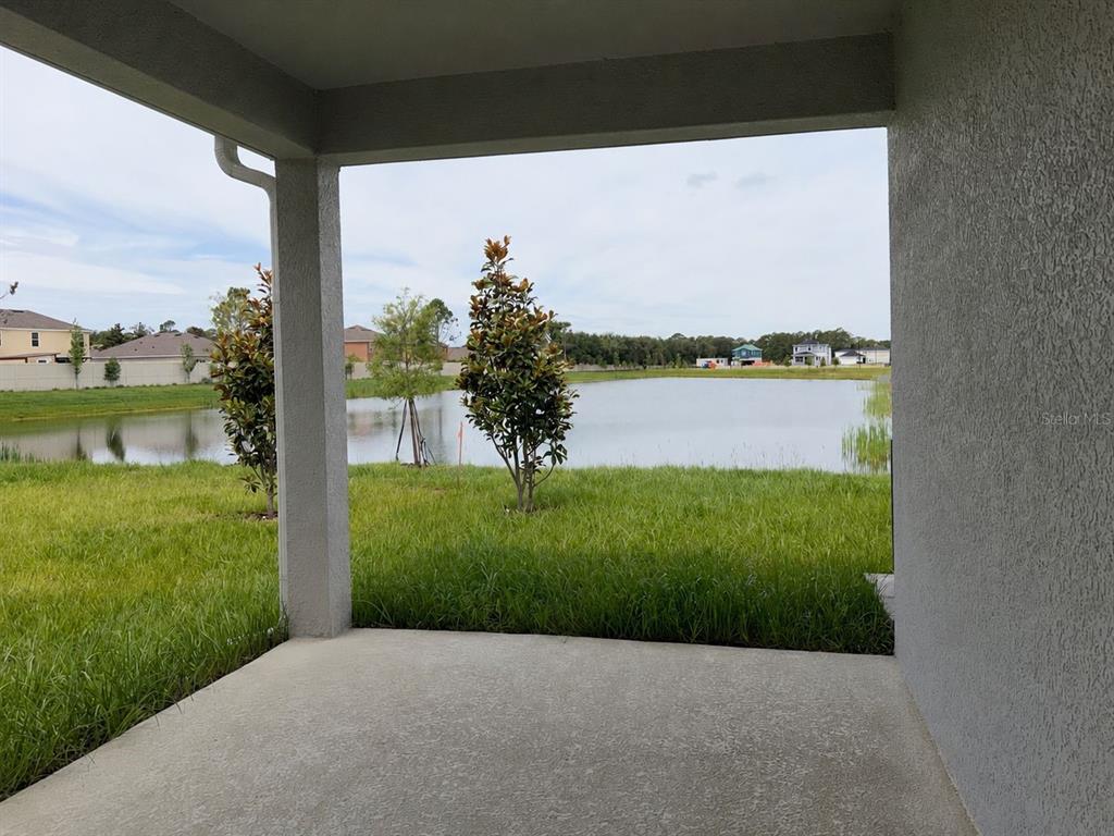 A covered concrete patio overlooks a grassy lawn and a small pond — 2717 RAINDROP RUN STREET, CLERMONT, FL