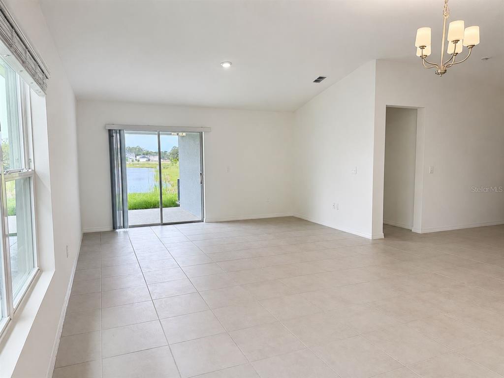 An empty room with light tile flooring, a sliding glass door, and a chandelier — 2717 RAINDROP RUN STREET, CLERMONT, FL