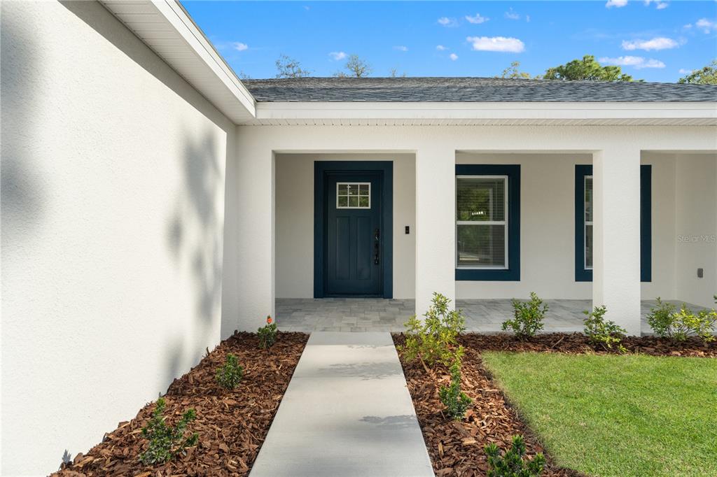 A concrete walkway leads to the covered front porch of a white house — 13025 KILDEER ROAD, WEEKI WACHEE, FL
