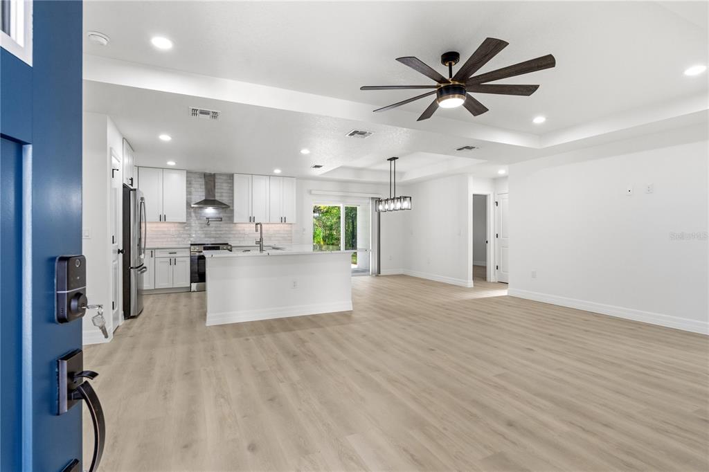 An open-concept kitchen and living area features white cabinetry, a central island, and wood-look flooring — 13025 KILDEER ROAD, WEEKI WACHEE, FL