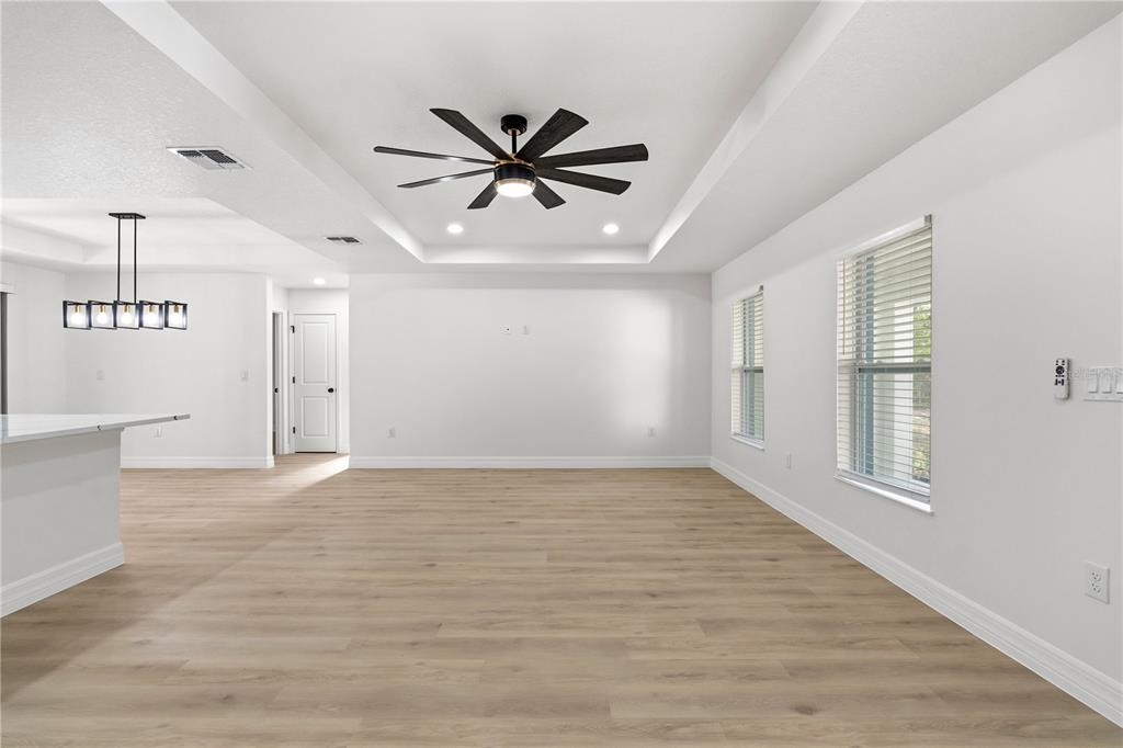 A bright living room features light wood-look flooring, a tray ceiling with a fan, and windows — 13025 KILDEER ROAD, WEEKI WACHEE, FL