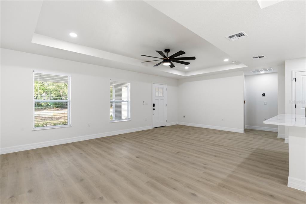 A spacious, empty living room features white walls, light wood-look flooring, and a tray ceiling — 13025 KILDEER ROAD, WEEKI WACHEE, FL
