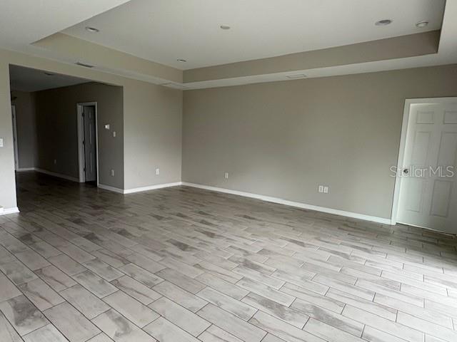An empty room features light-colored wood-look tile flooring, recessed lighting, and a tray ceiling — 5329 SENZA TRAIL, PALMETTO, FL