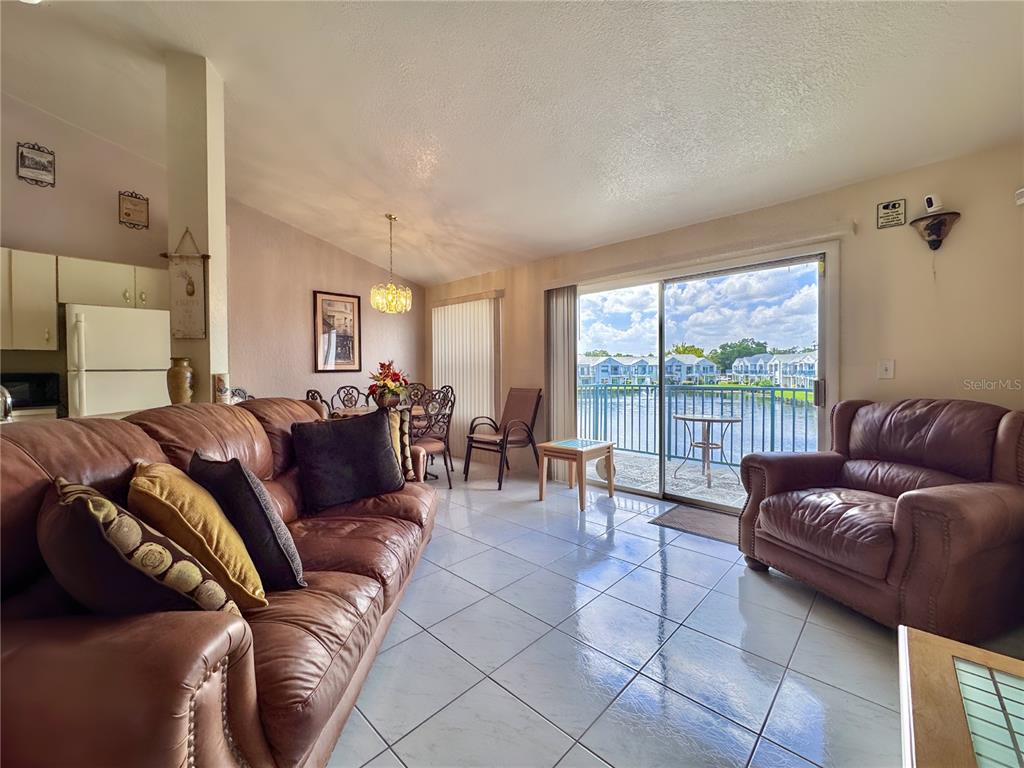 A living room with tile floors, leather furniture, and a sliding glass door overlooking water — 2520 WOODGATE BOULEVARD UNIT 202, ORLANDO, FL