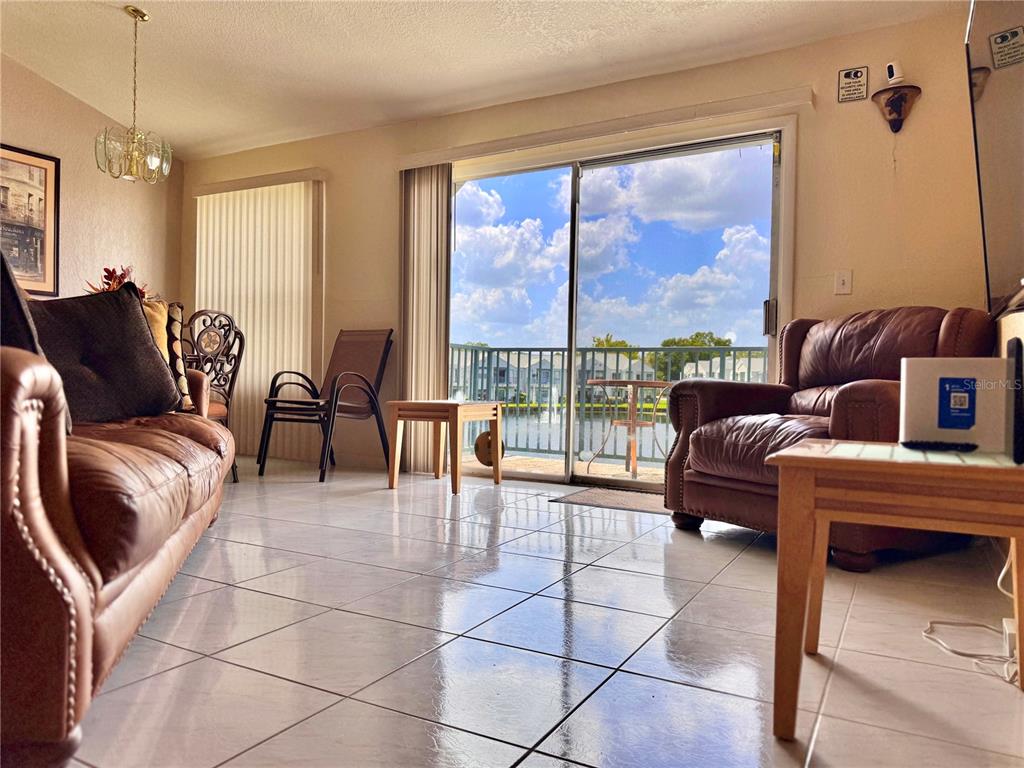 A living room with tile floors, leather furniture, and a sliding glass door overlooking a lake — 2520 WOODGATE BOULEVARD UNIT 202, ORLANDO, FL