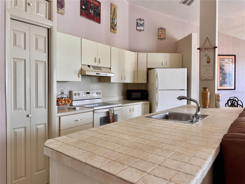 A kitchen features tiled countertops, white cabinets, a white stove, and a white refrigerator — 2520 WOODGATE BOULEVARD UNIT 202, ORLANDO, FL