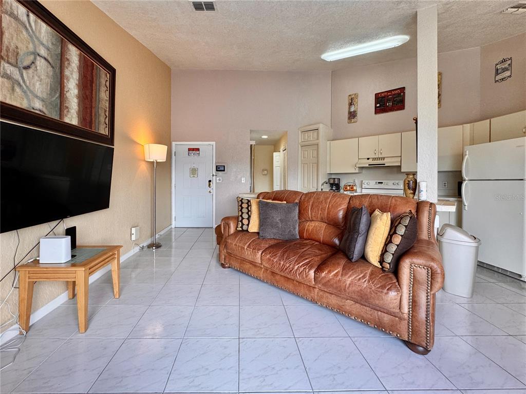 A living room with a leather sofa, tile flooring, and an open kitchen area — 2520 WOODGATE BOULEVARD UNIT 202, ORLANDO, FL
