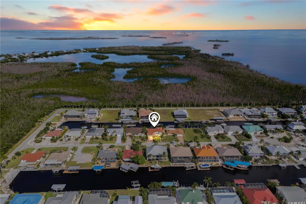 An aerial view shows a waterfront residential neighborhood with a canal and sunset horizon — 2420 CHERIMOYA LANE, ST JAMES CITY, FL