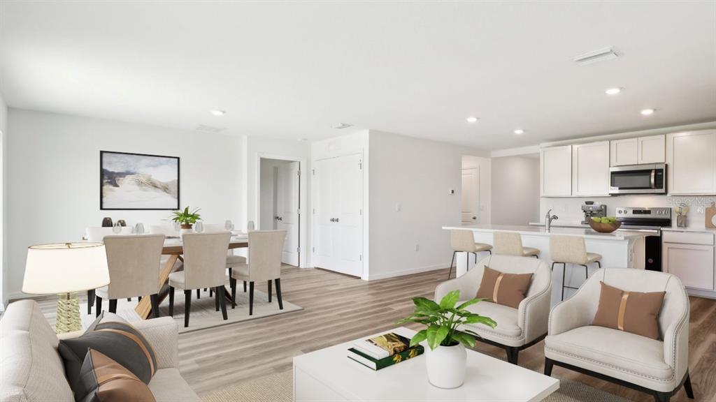 An open-concept living and dining area features light wood flooring, white walls, and modern furniture — 12322 HOPSCOTCH AVENUE, PARRISH, FL