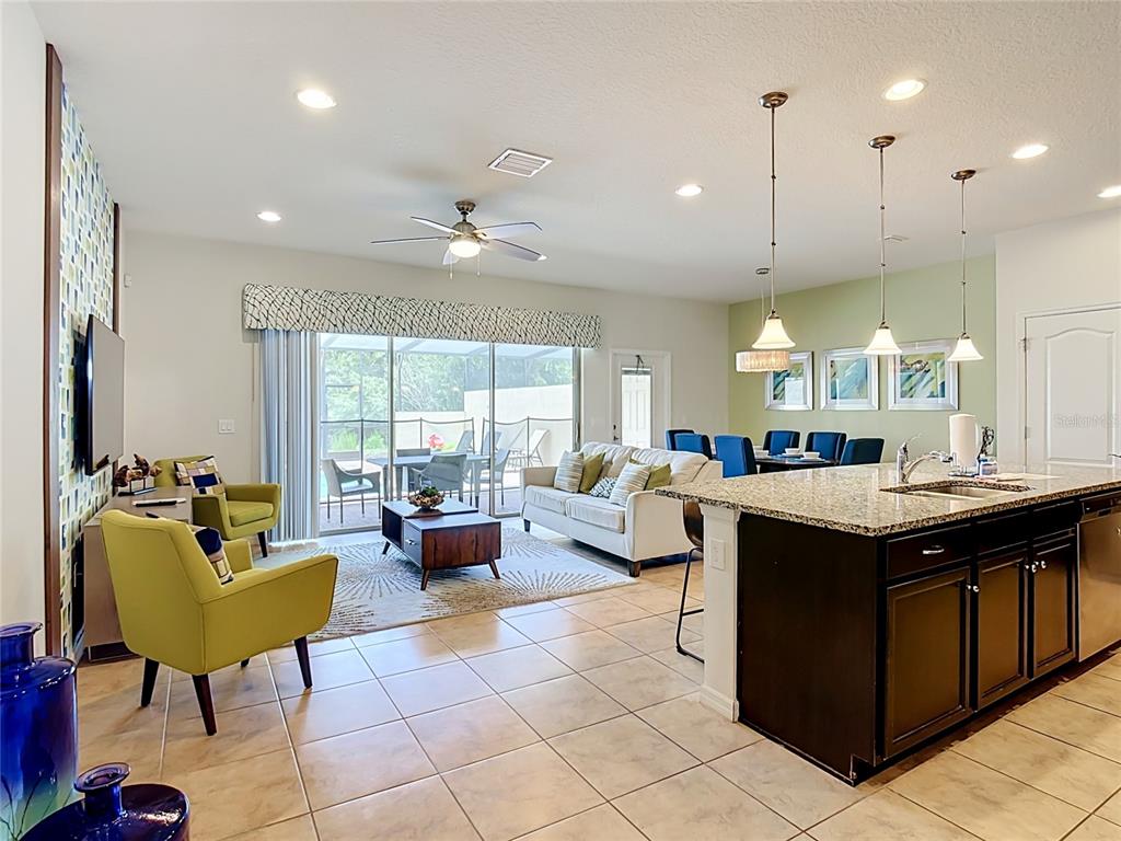An open-concept living and dining area features a kitchen island, tile floors, and patio access — 8899 GENEVE CT, KISSIMMEE, FL