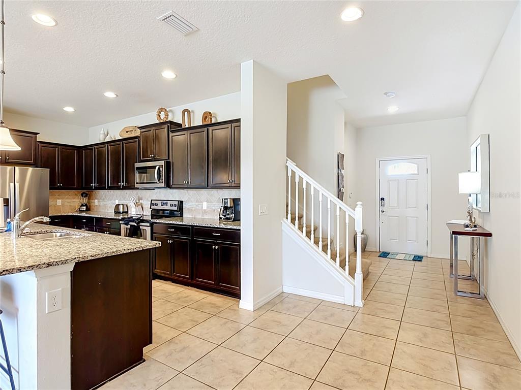 A kitchen with dark cabinets and granite countertops sits beside an entryway with stairs — 8899 GENEVE CT, KISSIMMEE, FL