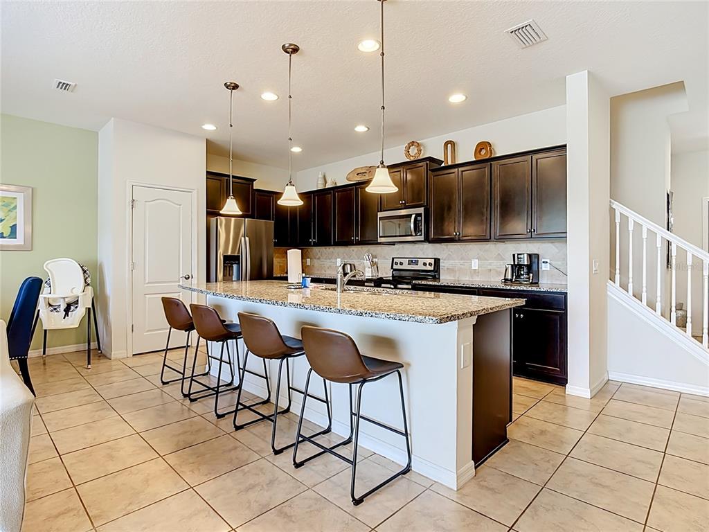 A kitchen features dark wood cabinets, granite countertops, a central island, and tile flooring — 8899 GENEVE CT, KISSIMMEE, FL