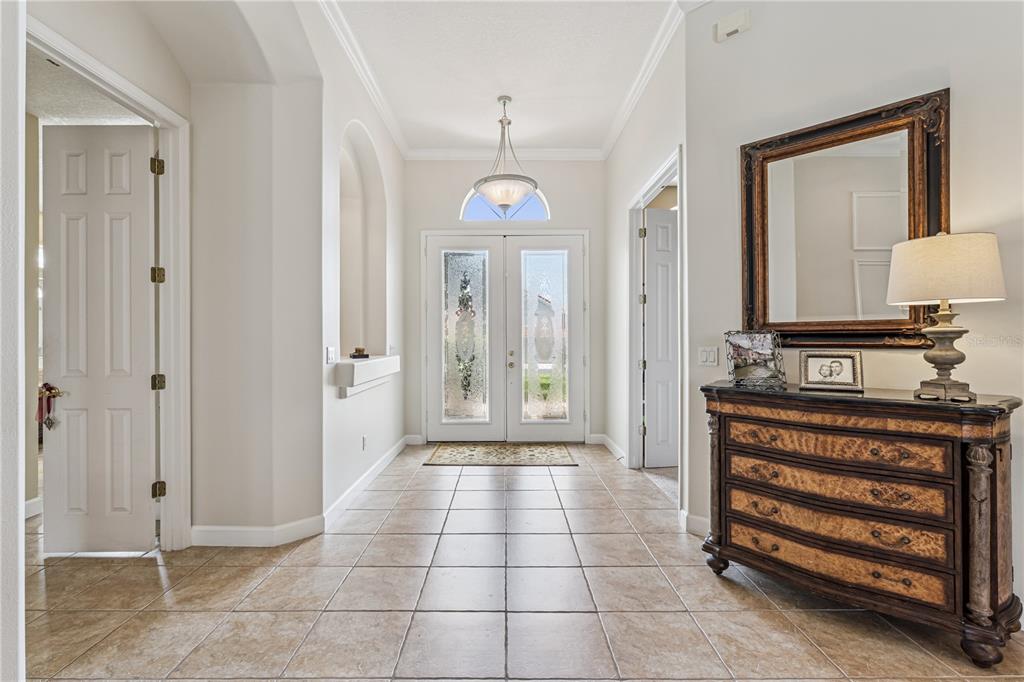 A tiled foyer features a double front door, a chandelier, and a wooden chest — 1949 DEERVIEW PLACE, LONGWOOD, FL