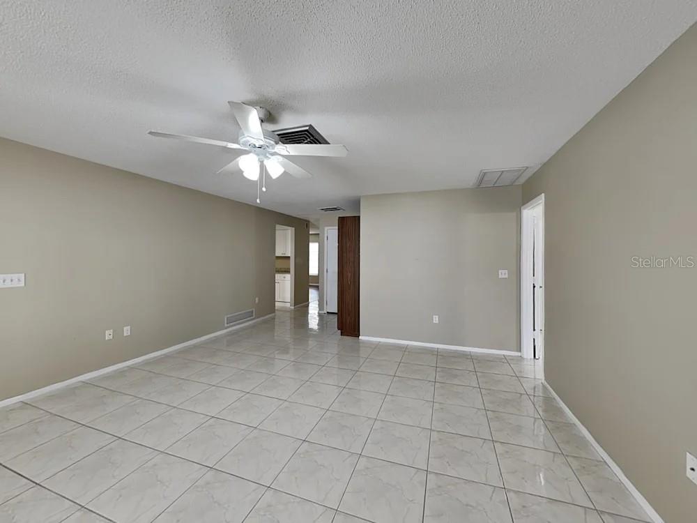 A living room with light-colored tile flooring, beige walls, and a ceiling fan — 8900 PHYLISS AVENUE, SARASOTA, FL