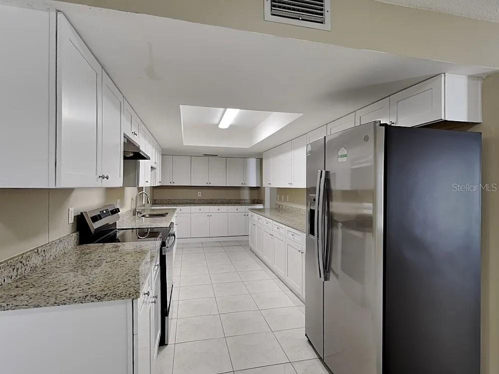 A galley kitchen features white cabinets, granite countertops, stainless steel appliances, and tile flooring — 8900 PHYLISS AVENUE, SARASOTA, FL