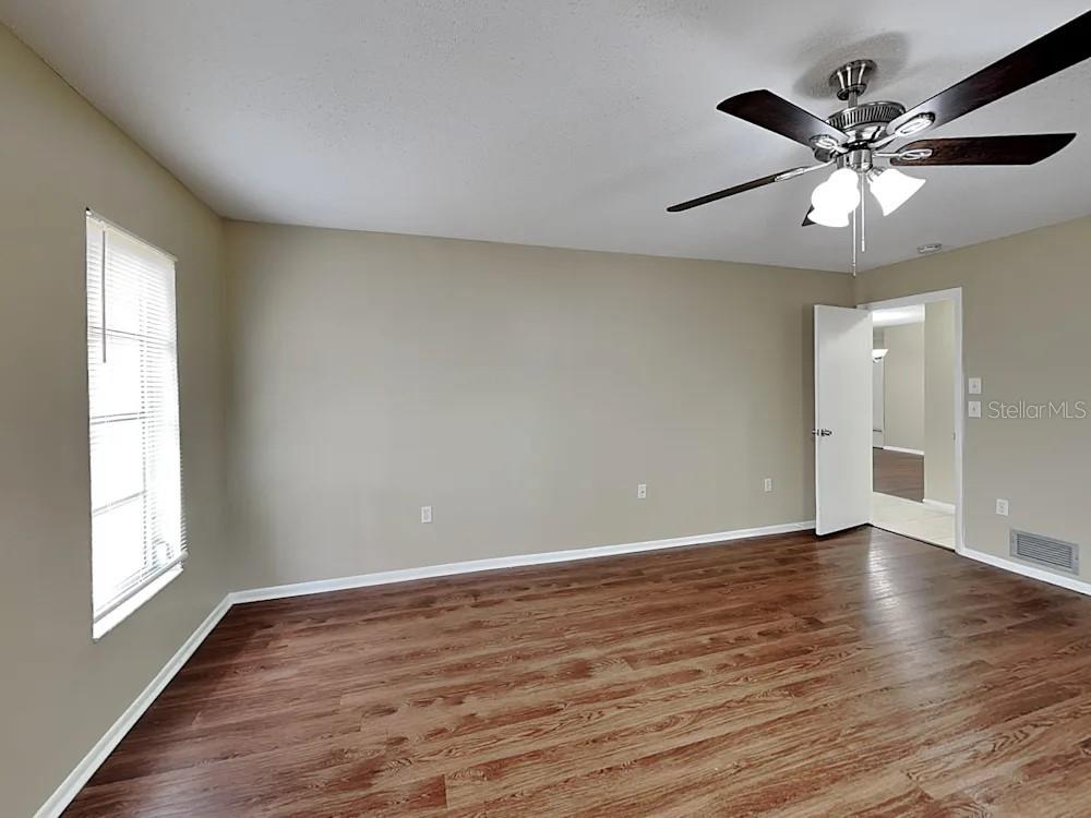 An empty room features wood-look flooring, beige walls, a ceiling fan, and a window — 8900 PHYLISS AVENUE, SARASOTA, FL