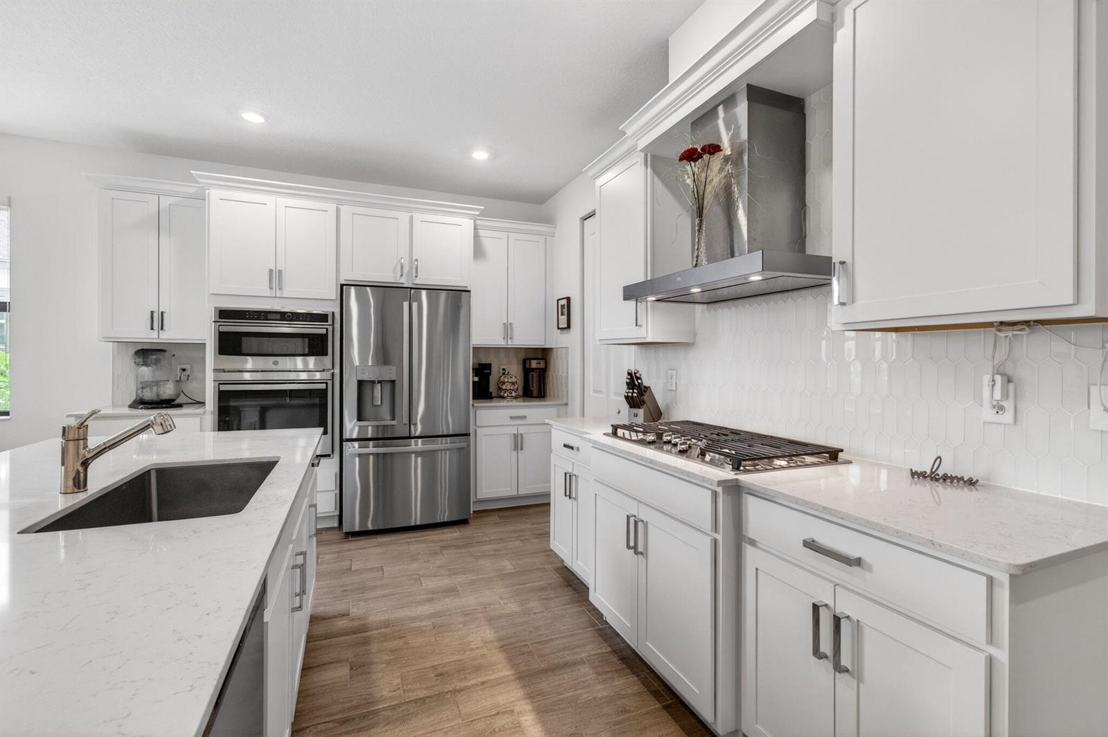 A modern kitchen features white cabinetry, stainless steel appliances, and a large quartz-topped island — 1136 Tangled Orchard Trace, Loxahatchee FL 33470, LOXAHATCHEE, FL