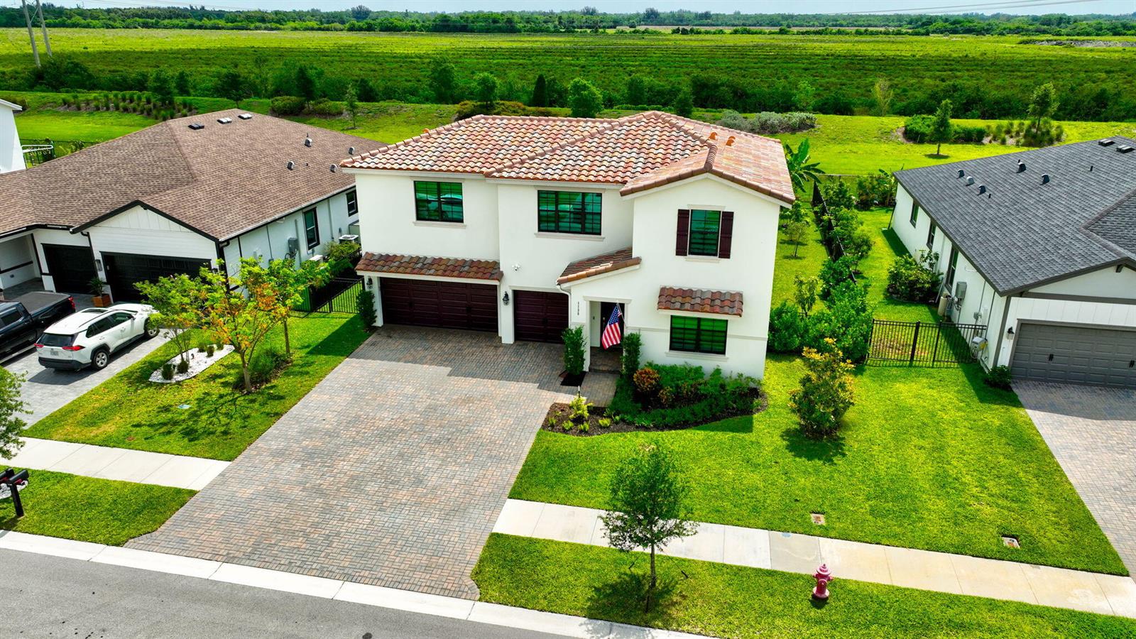 An aerial view of a two-story house with a tiled roof and a paved driveway — 1136 Tangled Orchard Trace, Loxahatchee FL 33470, LOXAHATCHEE, FL