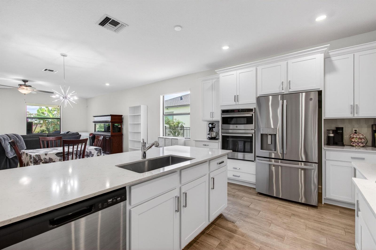 A modern kitchen features white cabinetry, stainless steel appliances, a large island, and wood-look flooring — 1136 Tangled Orchard Trace, Loxahatchee FL 33470, LOXAHATCHEE, FL