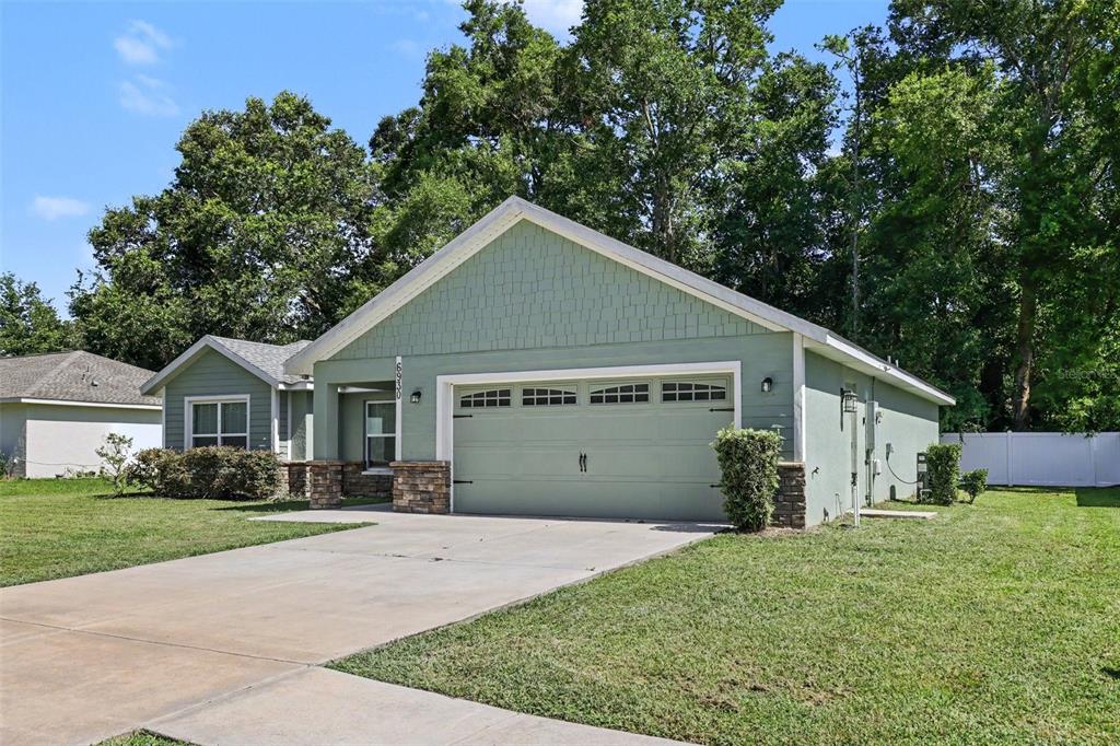 A light green house with a two-car garage and stone accents sits on a lawn — 6930 SW 109TH LANE, OCALA, FL