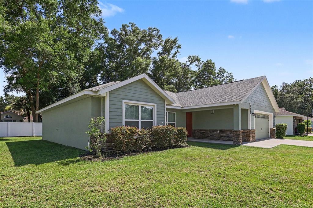 A single-story house with green siding, stone accents, a covered porch, and a two-car garage — 6930 SW 109TH LANE, OCALA, FL