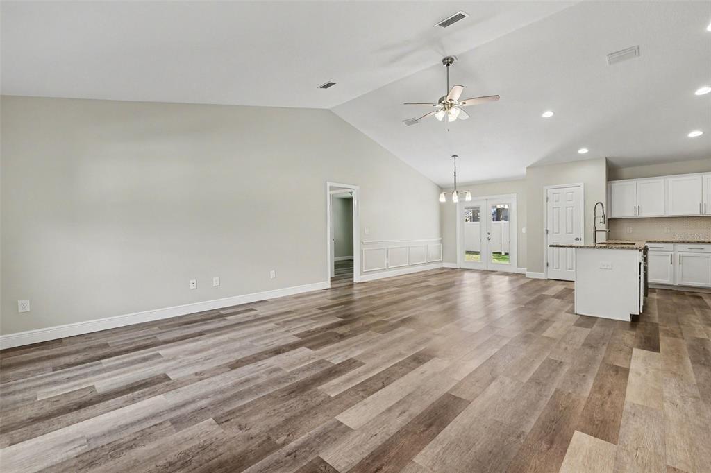 A spacious room with vaulted ceilings, wood-look flooring, and an open kitchen with white cabinets — 6930 SW 109TH LANE, OCALA, FL