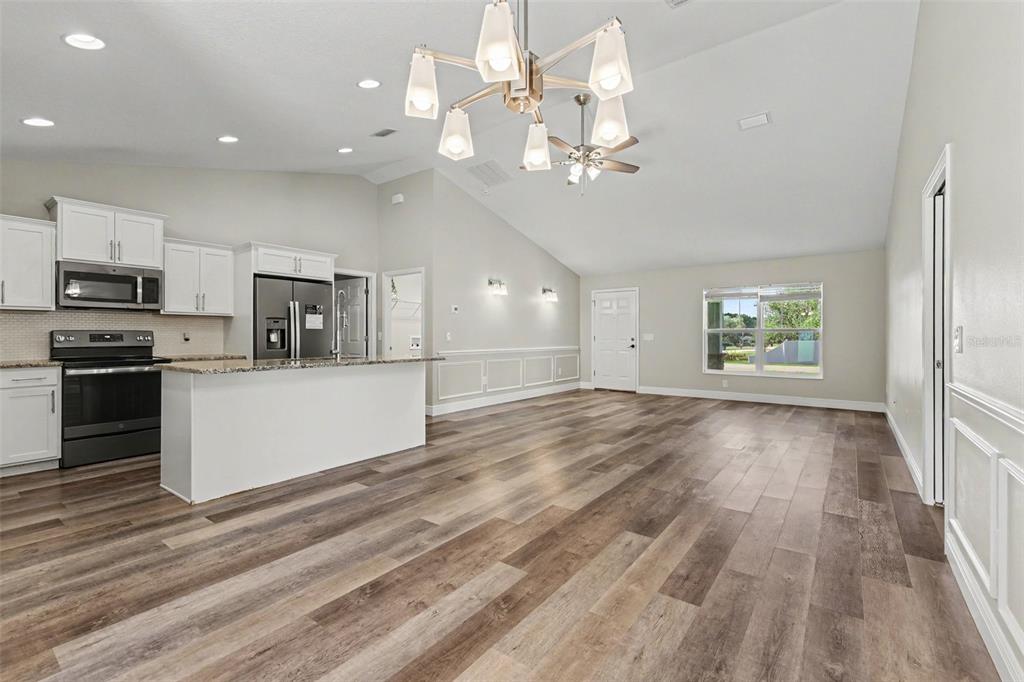An open-concept kitchen and living area featuring white cabinets, stainless appliances, and wood-look flooring — 6930 SW 109TH LANE, OCALA, FL