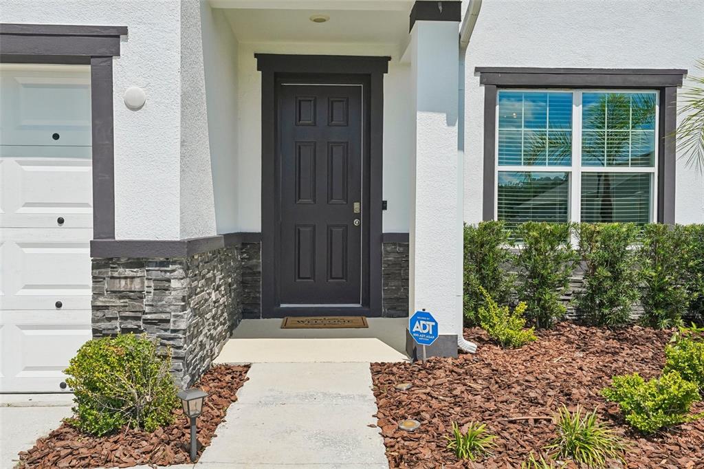 The exterior of a house features a dark front door, stone siding, and a walkway — 1297 BERING ROAD, WESLEY CHAPEL, FL