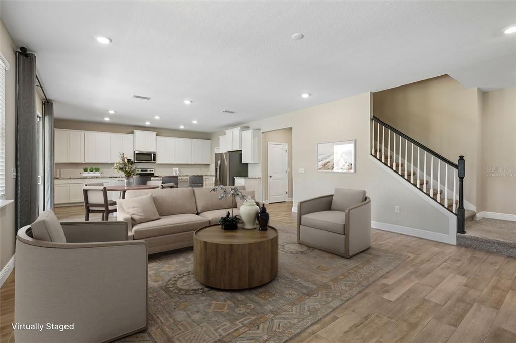 A virtually staged living room with wood-look flooring, a staircase, and an open-concept kitchen — 1297 BERING ROAD, WESLEY CHAPEL, FL