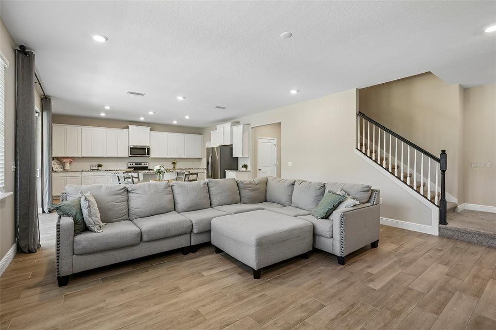 An open-concept living room features a large gray sectional sofa, wood-look flooring, and stairs — 1297 BERING ROAD, WESLEY CHAPEL, FL